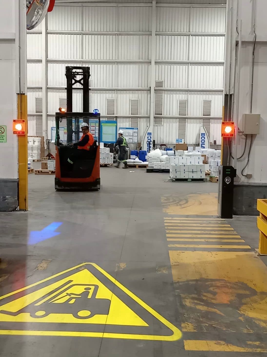 Señal de precaución para montacargas proyectada en el piso, junto a luces de advertencia